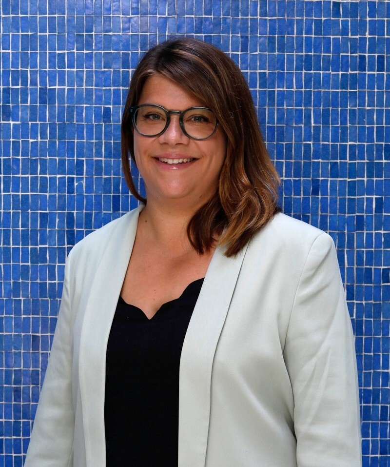 Ann-Kristin steht vor einer blauen Wand und lächelt