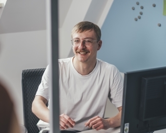 Ein Mann sitzt an seinem Bürotisch und unterhält sich mit einer Person, die sich außerhalb der Kamera befindet.