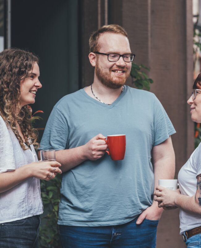 Drei Personen stehen draußen vor dem Haus des Buches und unterhalten sich bei einem Kaffee.